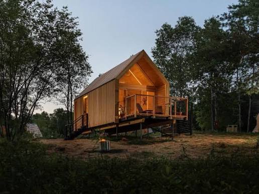 Elevated timber cabin glowing at dusk surrounded by trees